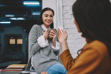 Surprised hipster girl amazed with information told by friend on coffee break, young woman wondering about news getting from female colleague explaining points and asking questions gesturing in office