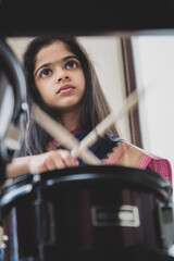 Fototapeta na wymiar British Indian girl practices the drums wearing a traditional saree or sari. 