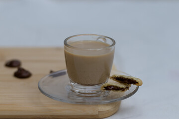 homemade butter cookies filled with chocolate flavored cream next to a full glass of instant coffee, against a wooden background