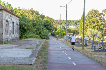 View of eco pedestrian / cycle lane, with men running and cycling, trees, house and work out machines as background
