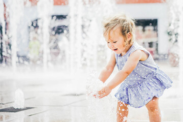 Happy little girl playing in a water fountain. Hot summer.