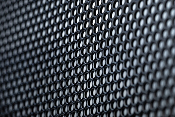 Macro shot of a black metal surface with round holes, gray background.