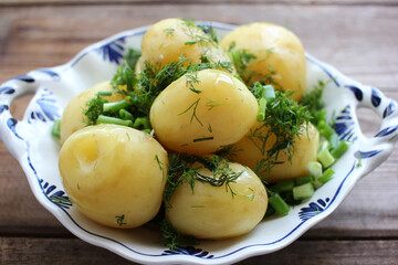 Traditional swedish midsummer food new potatoes with dill and light beer on old wooden board table. Whole boiled potatoes on the white plate
