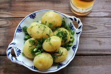 Traditional swedish midsummer food boiled potatoes with dill and chopped onion and light beer on the old wooden board table. Top view
