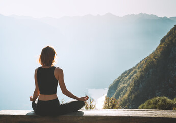 Young woman is meditating in mountains. - obrazy, fototapety, plakaty