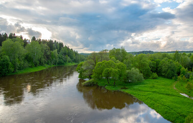 A dark river flows among green banks under a dark, cloudy sky.