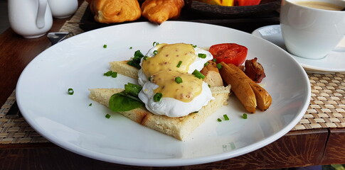 Poached eggs on two pieces of toast, sausage and tomato.