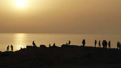 People watch the sunset near the ocean. A darkened image.