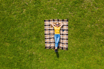 Top view young woman lying on the plaid blanket on green grass.