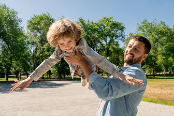 Happy young man holding his cute cheerful little son, lifting and whirling him