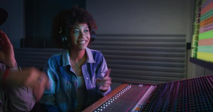 A professional male producer and young african female singer are happy with results of recording a new song and  are celebrating a future success in a music studio with colorful lights on a background