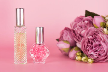 Different transparent perfume bottles with bouquet of peonies on pink background. Aromatic essence bottles with spring flowers. Perfumery, cosmetics, fragrance collection.