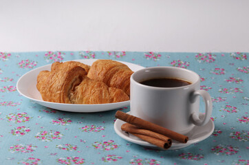 a white ceramic cup of coffee and a saucer with cinnamon sticks on vintage pattern textile surface