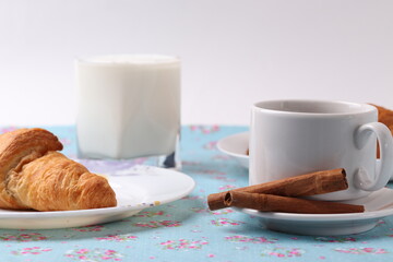 a white ceramic cup of coffee and a saucer with cinnamon sticks on vintage pattern textile surface