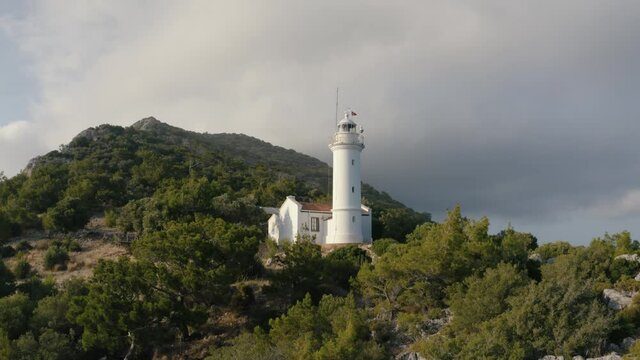Flying over a lighthouse on the hill. Mountains on the background covered by green trees. Turkey 4K