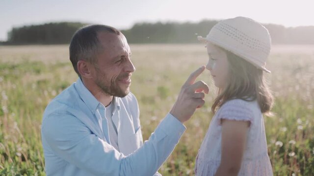 Father and daughter playing, touch the nose of each other on the field during sunset. A caucasian man and his daughter hug each other. Happy family.