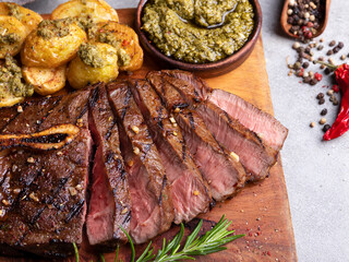 Sliced juicy grilled steak medium rare beef on bone roasted potatoes sauce pesto