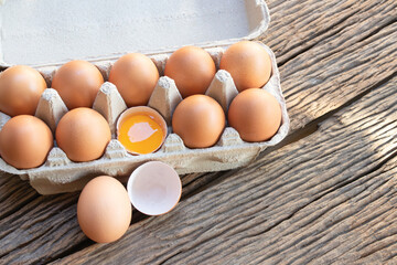 Chicken eggs, brown eggs, broken egg with yolk in carton box on wooden rustic table. Top view eggs in carton box.