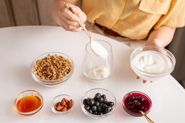 Young woman making yoghurt with honey, berries, jam and almond for breakfast