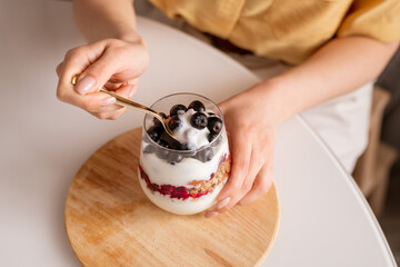 Hands of young female with teaspoon eating tasty homemade youghurt by table