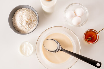 Overview of glass bowls with eggs, honey, dough for pancakes, sourcream, flour