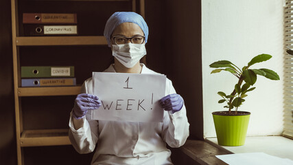Healthcare worker demonstrate slogan ONE week. Woman in medical uniform holds countdown sign....
