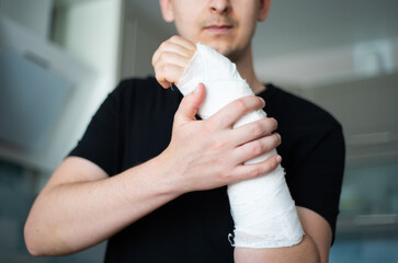 A young man checks the plaster bandage for strength by touching a broken arm close-up