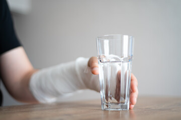 A man with a broken bone tries to take a glass of water. Disability. Bandage on the wrist