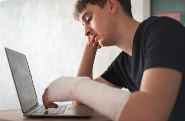 A man with an arm injury looks into a laptop. Online diagnosis. Health insurance