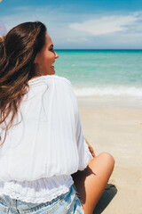 View from the back of a young smiling girl sitting on the seashore near the sea. The concept of travel and rest