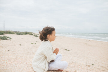 Naklejka na ściany i meble Young caucasian girl meditate at the beach, doing yoga lotus pose, child meditation outdoors