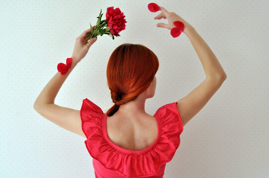 Redhead girl dancing with a red peony and petals on her hands