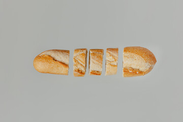 A flat lay of a baguette bread cut up on a light pastel grey background
