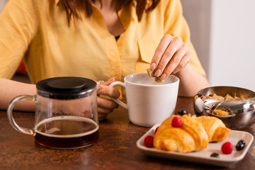 Hands of young woman putting brown sugar into cup with tea or coffee