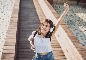 Young beautiful woman listening to music, having fun and enjoying life, Excited girl holding smartphone in a city. Student lifestyle, emotions, technology, people concept