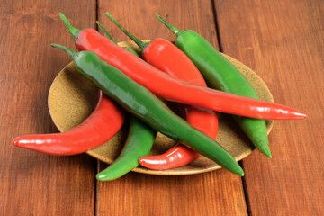 Red and green chili peppers lie strewn on a plate on a wooden table