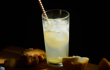 Fototapeta na wymiar Lemonade in glass with ice cubes. Summer refreshing drink banner. Lemon peel and ginger root. Black background on wooden desk. Copy space
