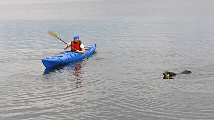 Fototapeta na wymiar Young man kayaking with dog on big lake. Summer. Finnish Lapland