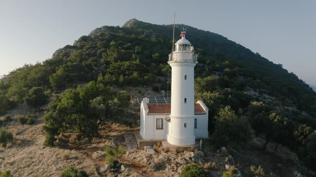 Flying over a lighthouse on the hill. Mountains on the background covered by green trees. Turkey 4K