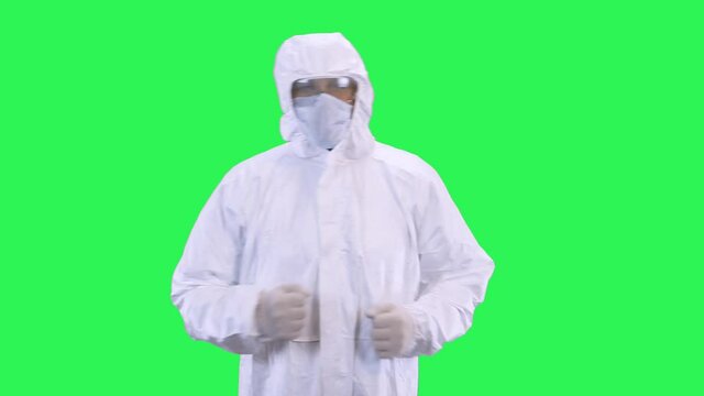 A man in a protective suit with a mask on his head and glasses goes forward on a green background