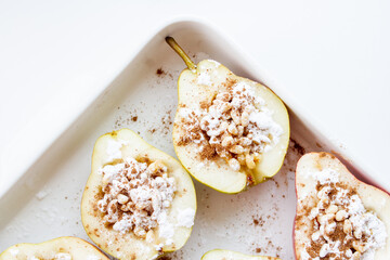 Stuffed pears dessert in white baking dish. Halves of pears with nuts, cinnamon and icing sugar. Dessert recipe