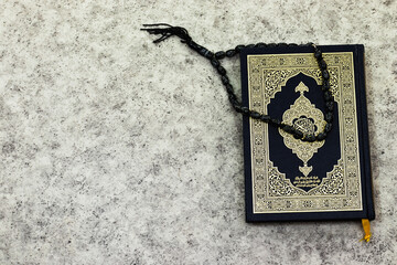 Holy Quran with Arabic calligraphy meaning of Al Quran and black rosary