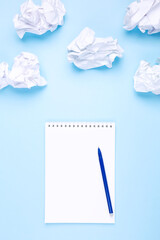 White notebook and pen on blue background around crumpled paper in the form of clouds. Concept of drawing up wish list and dreams, head in the clouds