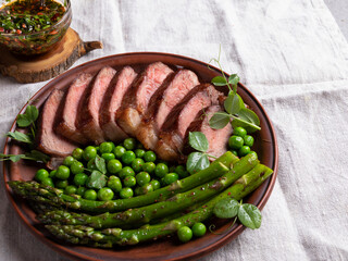juicy roasted beef chopped steak, with green peas, roasted asparagus, on plate close up