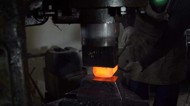 Blacksmith Holding Big Heated Piece of Iron in Tongs While Using Forging Press. Hydraulic Hammer Shaping Red-hot Metal