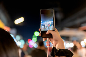 People using mobile phones Photographing tourists In the night market which travel attractions in Thailand, to technology and application concept.