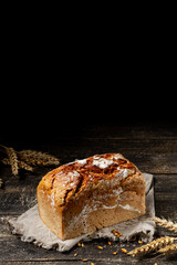 Loaf of black bread with seeds on textile towel on rustic wooden texture background. Vertical composition with copy space