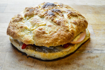 Little italian focaccia bread stuffed with turkey ham, red bell peppers, cheese and red onions on wooden cutting board, close up.