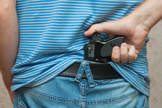 A man hold the loaded gun behind the belt.