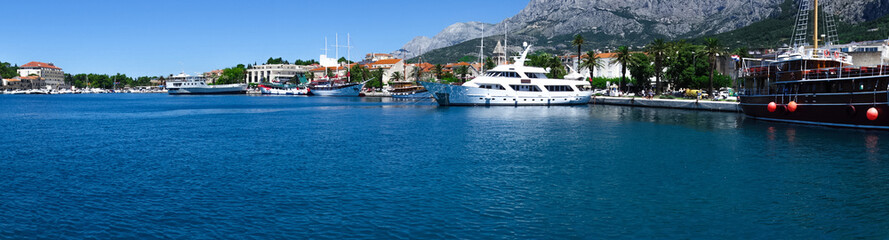 Chorwacja Makarska zdjęcie panoramiczne wykonane z morza. Widok na przystań, promenadę, stare miasto. Na pierwszym planie jacht i wycieczkowy statek.